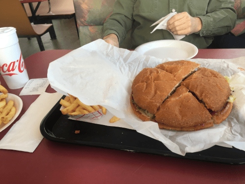 A large sandwich cut into quarters on a tray, accompanied by fries and a drink in a fast-food setting.