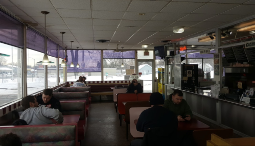 A cozy diner interior with booths, customers seated, and a snowy view outside through large windows.
