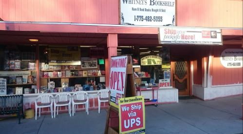 Exterior of Whitney's Bookshelf, featuring a sign for shipping services and a display of used books in the window.