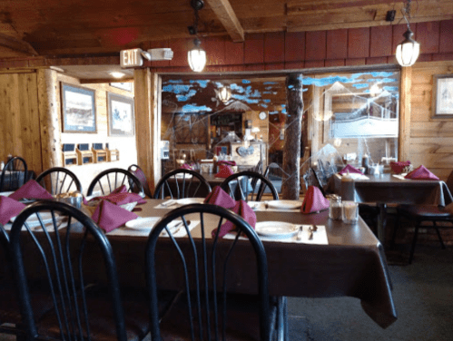 Cozy restaurant interior with wooden decor, tables set with maroon napkins, and a rustic ambiance.
