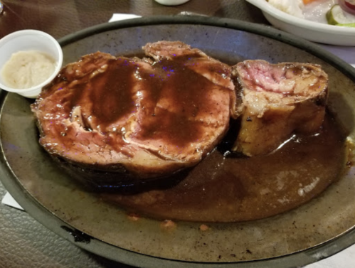 A plate of juicy prime rib with a rich brown sauce, served with a small cup of horseradish on the side.
