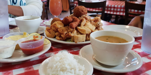 A table set with a large plate of fried seafood, a bowl of soup, rice, and dipping sauces in a cozy restaurant.