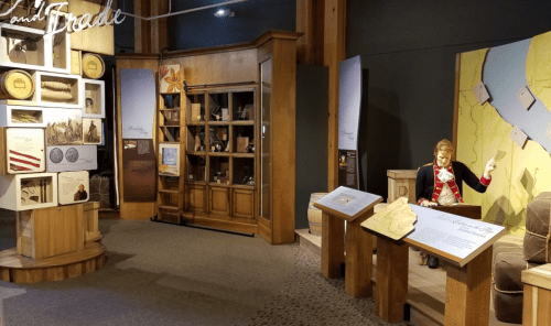 A museum exhibit featuring displays, artifacts, and a figure interacting with a map in a wooden setting.