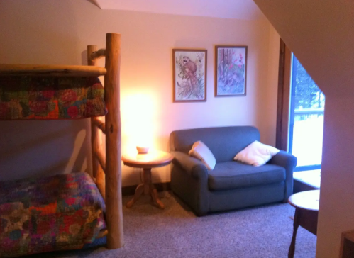 Cozy room with a bunk bed, sofa, and a side table, illuminated by warm light from a nearby window.