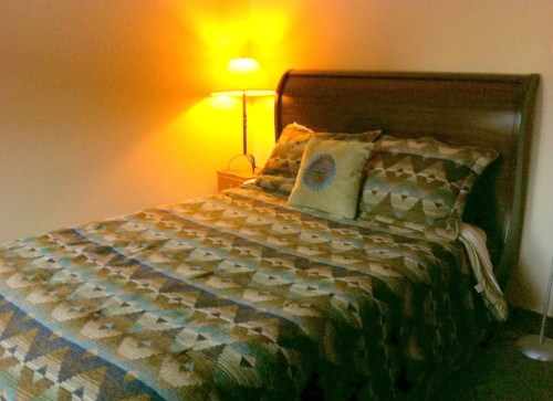 Cozy bedroom with a wooden bed, patterned quilt, and a warm lamp casting a soft glow.