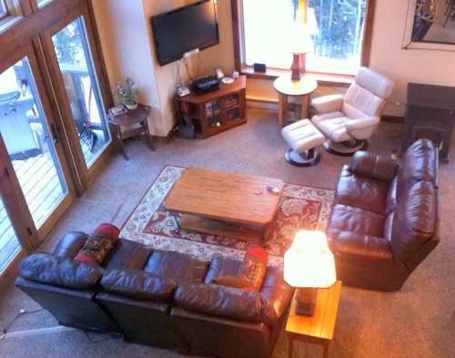 Cozy living room with a leather sofa, armchair, wooden coffee table, and large windows overlooking a snowy landscape.