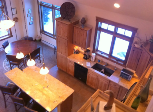 A cozy kitchen and dining area with wooden cabinets, a large island, and windows overlooking a snowy landscape.