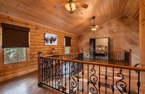 Interior of a rustic log cabin featuring wooden walls, a balcony with decorative railing, and warm lighting.