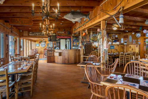 Cozy wooden restaurant interior with tables, a bar, and nautical decor, featuring a large fish hanging from the ceiling.