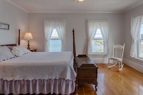 Bright bedroom with a large bed, rocking chair, and windows overlooking a scenic view of the water.