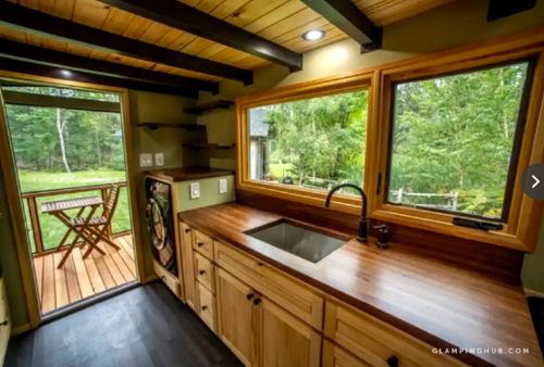 Cozy kitchen with wooden cabinets, sink, and large windows overlooking a green outdoor space.