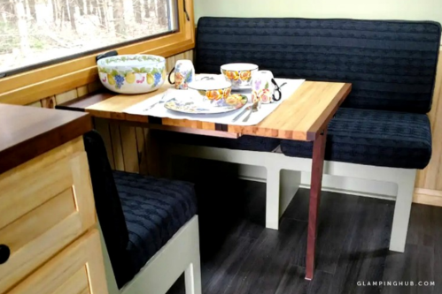 Cozy dining area with a wooden table, two upholstered benches, and colorful dishware in a cabin setting.