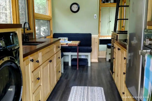 Cozy interior of a tiny home featuring a kitchen, dining area, and wooden cabinetry with large windows.