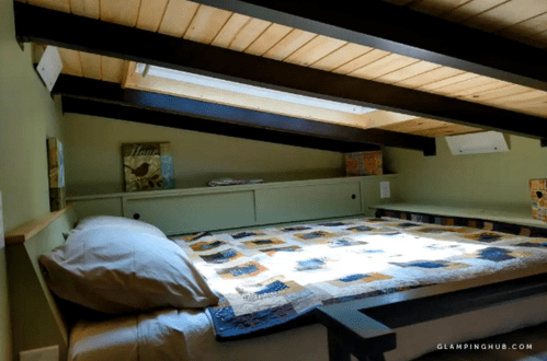 Cozy loft bedroom with a quilted bedspread, wooden ceiling, and natural light from skylights.