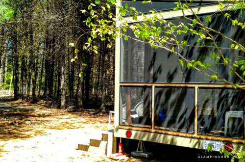 A cozy glamping cabin surrounded by trees, featuring a screened porch and steps leading to the entrance.