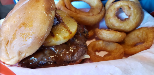 A juicy burger with grilled pineapple and barbecue sauce, served with crispy onion rings on the side.