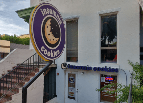 Exterior of Insomnia Cookies shop with a large sign featuring a cookie and the text "Open" in the window.