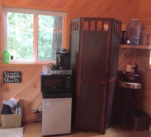 Cozy cabin interior featuring a mini fridge, coffee maker, wooden sink, and a window with forest views.
