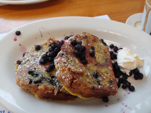 Two slices of blueberry French toast topped with powdered sugar, fresh blueberries, and a dollop of whipped cream.