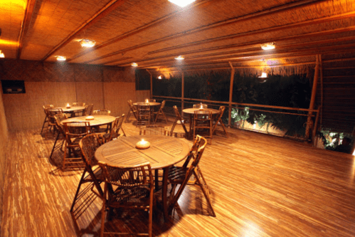 A cozy, dimly lit restaurant interior with wooden tables and chairs, featuring bamboo decor and warm lighting.
