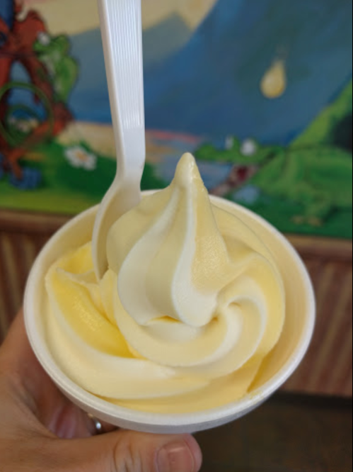 A hand holding a cup of soft-serve ice cream with a swirl of yellow and white flavors.