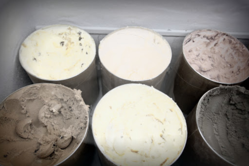 Six metal containers of various ice cream flavors, including chocolate, vanilla, and a light gray option.