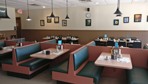 A cozy diner interior with green booths, tables set for dining, and wall art in a warm, inviting atmosphere.