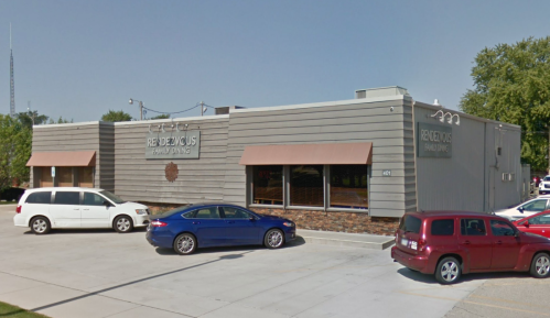 A modern building with a sign reading "Rendezvous" and parked cars in front on a clear day.