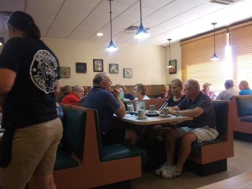 A busy diner scene with patrons seated at tables, chatting and enjoying meals, while a server attends to customers.