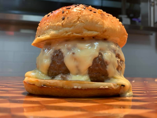 A close-up of a juicy burger with melted cheese, served on a sesame seed bun, resting on a wooden surface.