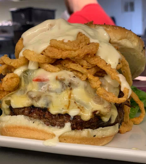 A close-up of a juicy burger topped with melted cheese, pickles, crispy onions, and creamy sauce, served on a bun.