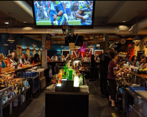 A lively bar scene with patrons, colorful drinks, and a TV showing a sports game in a vibrant atmosphere.