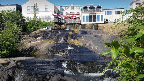 A scenic view of a rocky waterfall with a restaurant in the background, surrounded by greenery and blue skies.