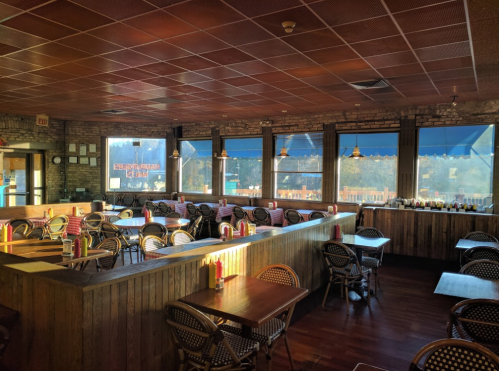 Cozy restaurant interior with wooden decor, empty tables, and large windows letting in natural light.