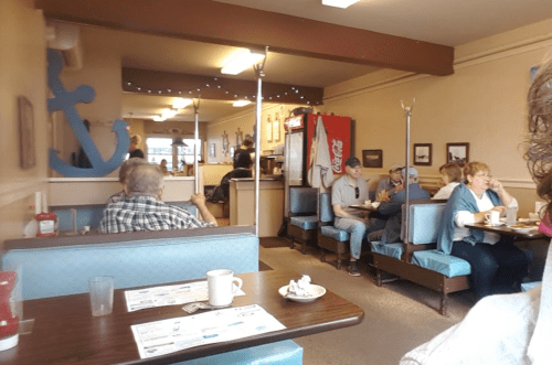 A cozy diner with blue booths, patrons enjoying meals, and nautical decor in a warm, inviting atmosphere.
