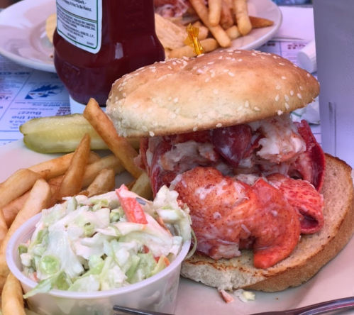 A lobster sandwich on a sesame seed bun, served with fries and coleslaw on the side.