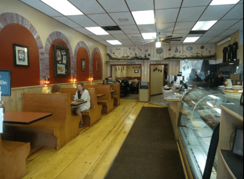 Cozy restaurant interior with wooden booths, a dessert display, and patrons enjoying meals in a warm atmosphere.