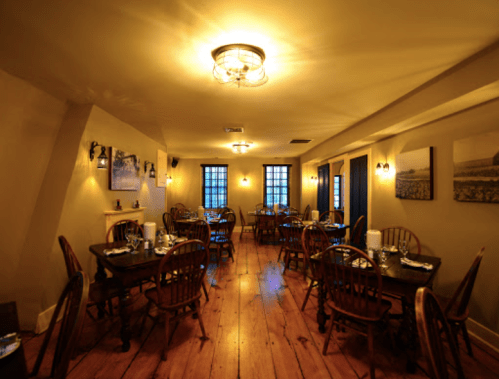 Cozy restaurant interior with wooden floors, tables set for dining, and warm lighting.