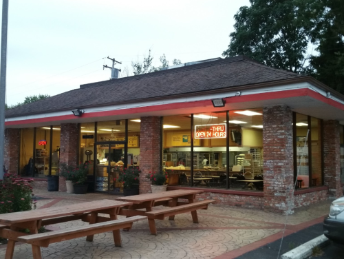 A brick building with large windows, featuring a neon "Open 24 Hours" sign and outdoor seating.