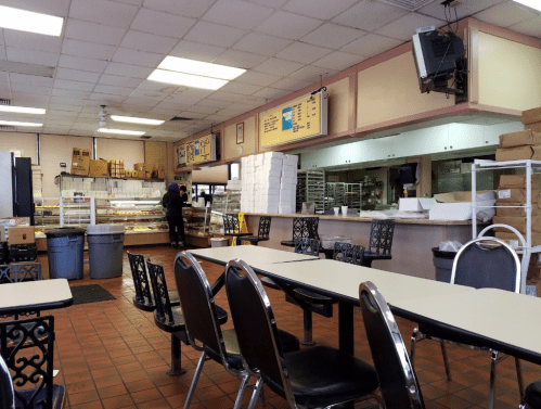Interior of a bakery with tables, a display case of pastries, and a staff member behind the counter.