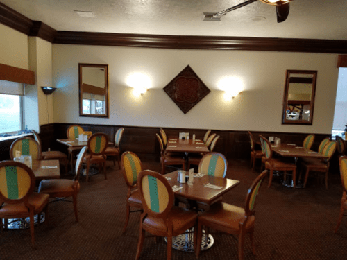 A cozy restaurant interior with wooden accents, round tables, and colorful chairs, featuring mirrors on the walls.