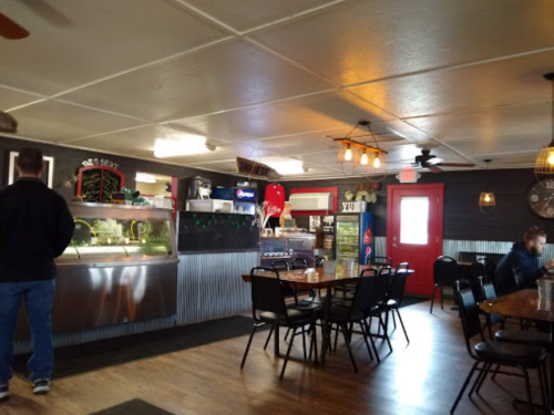 Interior of a casual restaurant with tables, a counter, and a red door, featuring a cozy atmosphere and rustic decor.