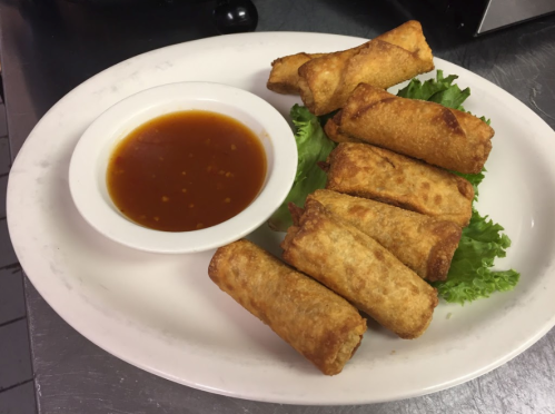 A plate of crispy spring rolls served with a small bowl of dipping sauce and garnished with lettuce.