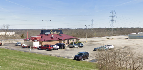 A restaurant with a red roof and sign, surrounded by a parking lot and power lines in the background.