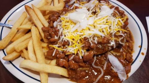 A plate of chili topped with cheese and onions, served with a side of crispy French fries.