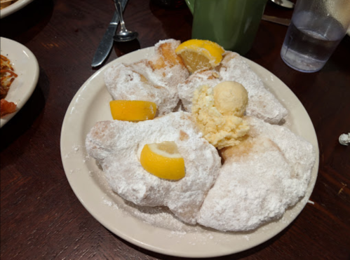 A plate of powdered sugar-covered beignets topped with lemon slices and a scoop of butter.