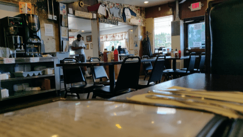 A cozy diner interior with empty tables, a coffee machine, and a person standing in the background.