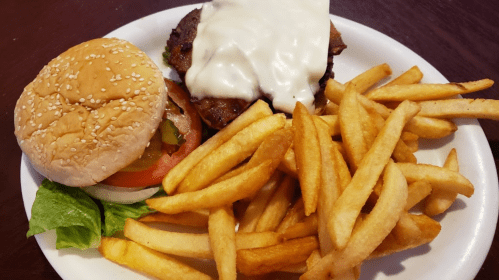 A plate with a cheeseburger, lettuce, tomato, pickles, and a side of golden French fries.