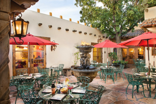 Outdoor dining area with green chairs, red umbrellas, a fountain, and a warm, inviting atmosphere.