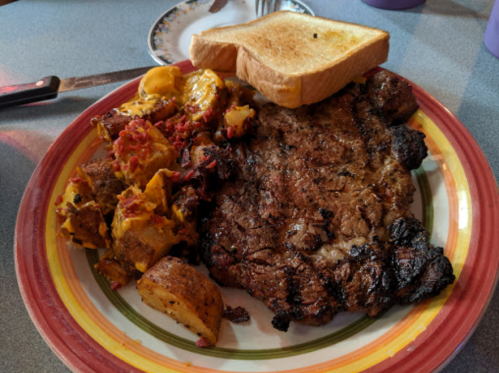 A plate with a grilled steak, golden toast, and seasoned potatoes with vegetables.